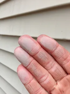 Hand showing chalky oxidation residue wiped from faded vinyl siding on a house